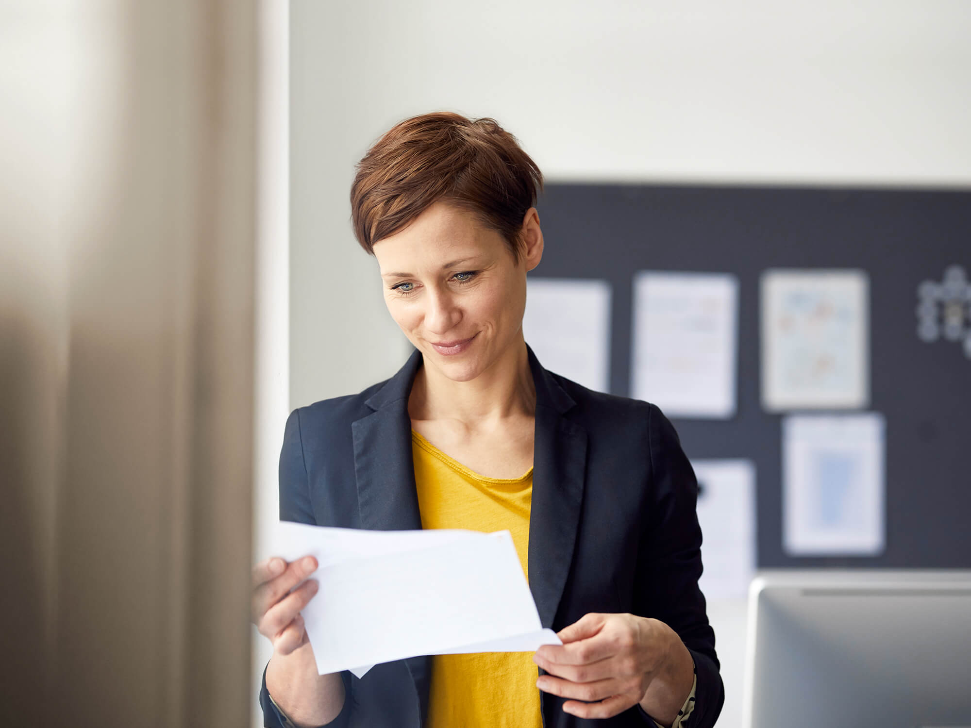 Une femme dans un bureau lit un document en souriant.